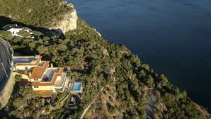 An aerial view of a coastal property with a swimming pool, terraced buildings, and a cliff overlooking the sea. - Coastline Arrabida Villa by Cadenzalux (Sesimbra)
