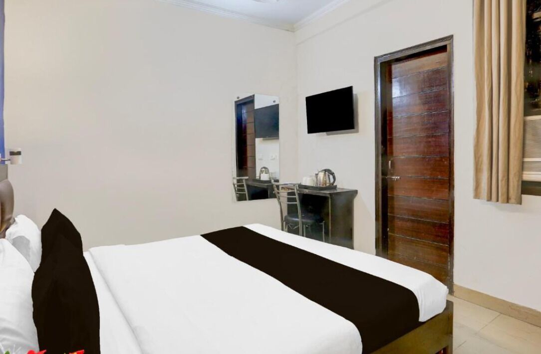 A hotel room with a bed, a desk, a chair, a television, and a door.