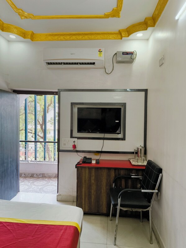 A hotel room with a bed, a desk with a chair, a TV mounted on the wall, and an air conditioning unit. - Hotel Dream (Patna)