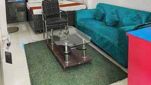 A compact hotel room with a bed, a teal sofa, a glass coffee table, and a small desk. - Hotel Dream  (Patna)