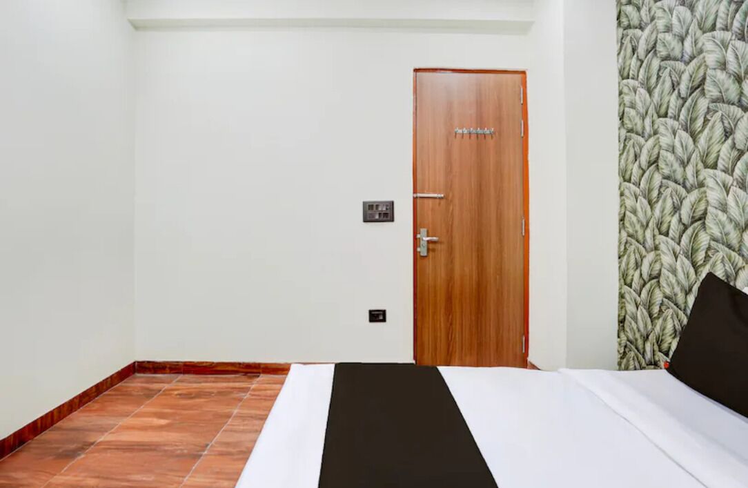 Una habitación de hotel con una puerta de madera, una cama con ropa de cama blanca y negra, y un papel tapiz estampado.