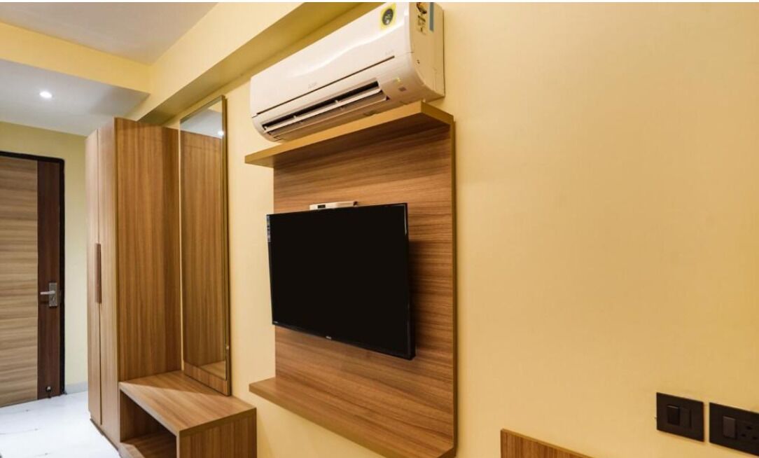 A room with a mounted TV, built-in shelving, and an air conditioning unit.