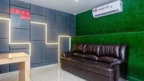 A modern lobby with a leather sofa, a wooden table, and a green wall with a mounted air conditioning unit. - Hotel Dream  (Patna)