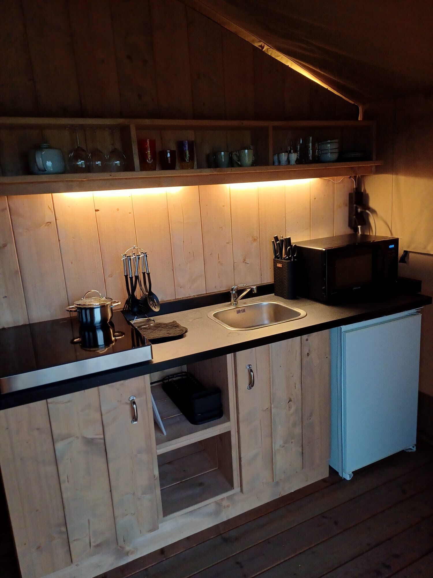 Una cocina compacta con armarios de madera, un lavamanos doble y un microondas.