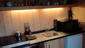 Una cocina compacta con armarios de madera, un lavamanos doble y un microondas.