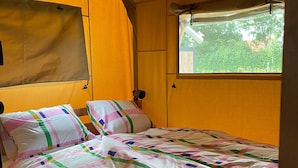 Una cama individual con un colcha colorida, una ventana con vistas a la vegetación y una pared amarilla.