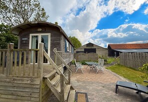 A rustic wooden building with a porch and a small outdoor seating area with metal chairs.