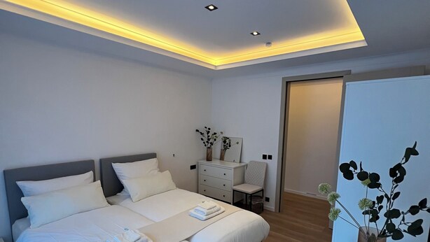 A modern bedroom with a large bed, bedside tables, a desk, and a chair.