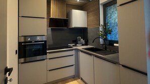 A modern kitchen with built-in appliances, a wooden slatted ceiling, and a window with a view.