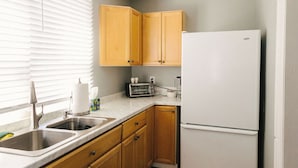 A kitchen with wooden cabinets, a white refrigerator, a sink, and a window with blinds.