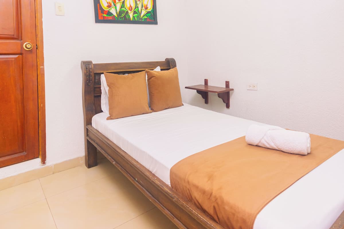 Un dormitorio con una cama de madera, una mesita de noche pequeña, un estante en la pared y un ventilador de techo.