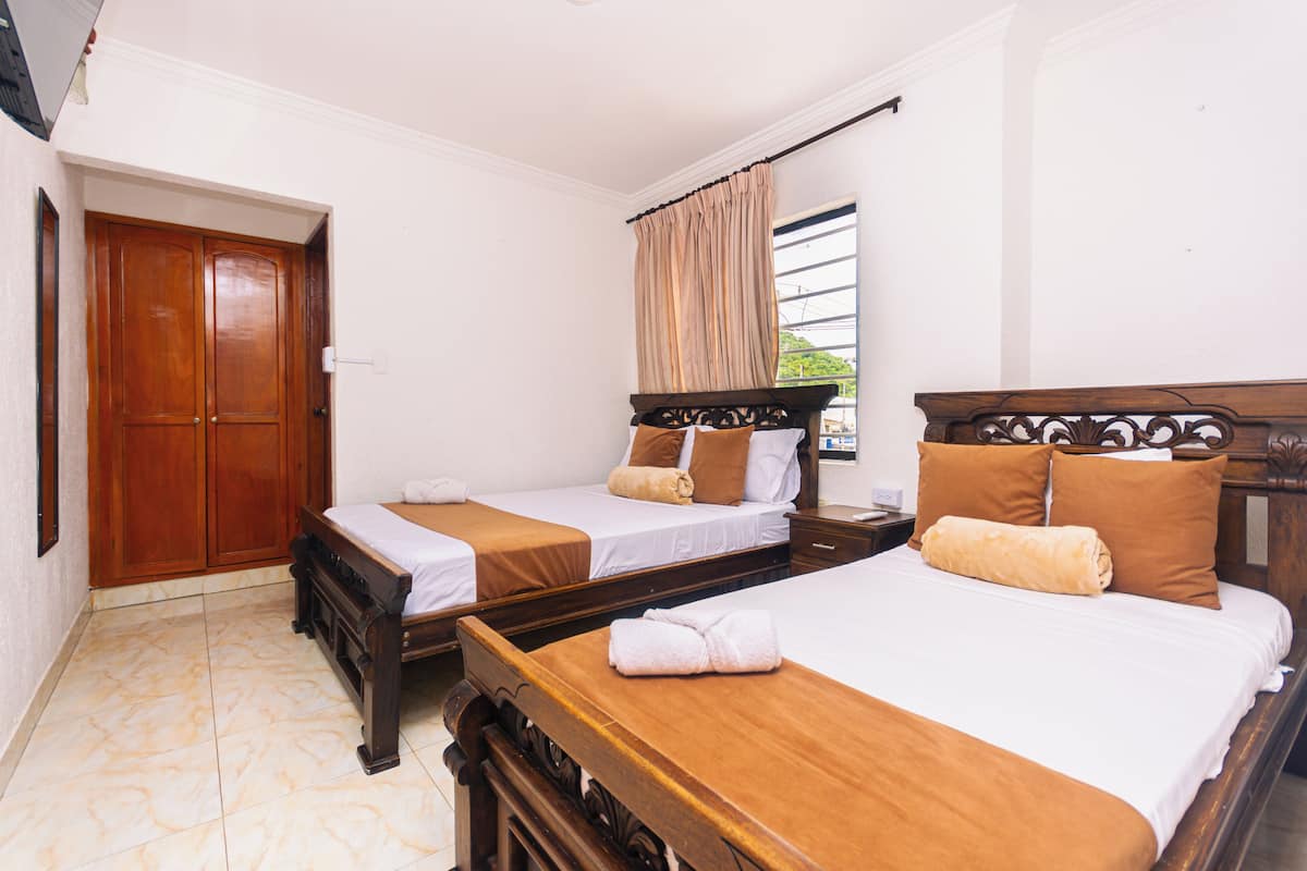 Una habitación de hotel con dos camas de madera, cortinas color beige y un armario de madera.