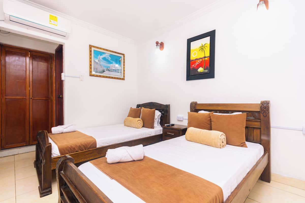 Una habitación de hotel con dos camas de madera, un armario, un cuadro y un equipo de aire acondicionado.