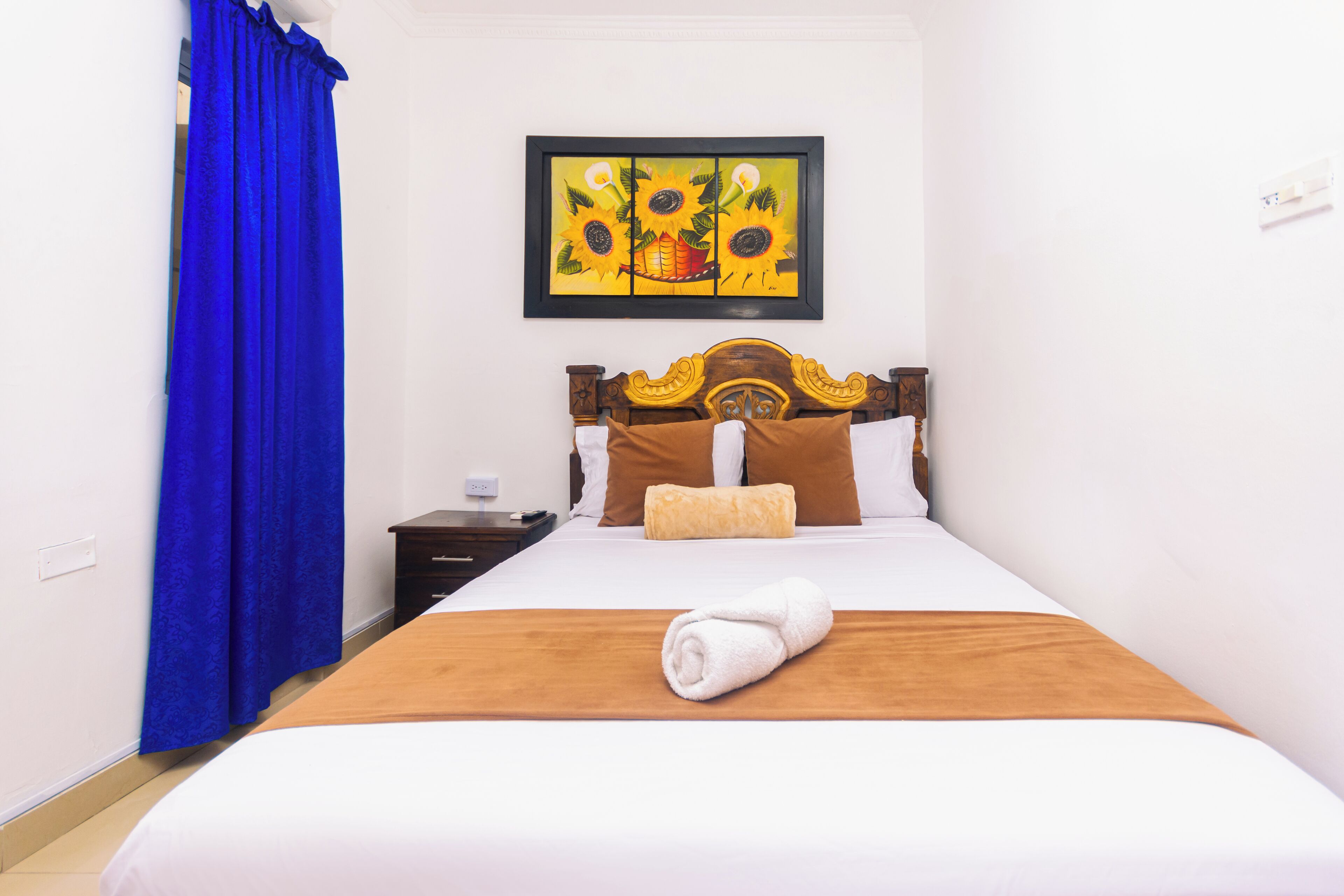 A neatly made bed with a brown headboard, white bedding, and a rolled white towel on the bed.