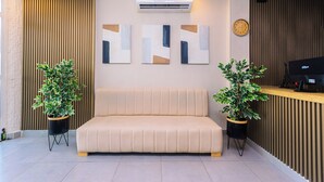 A reception area with a beige sofa, two potted plants, abstract wall art, a clock, and an air conditioning unit. - Hotel Med Cartagena (Cartagena)