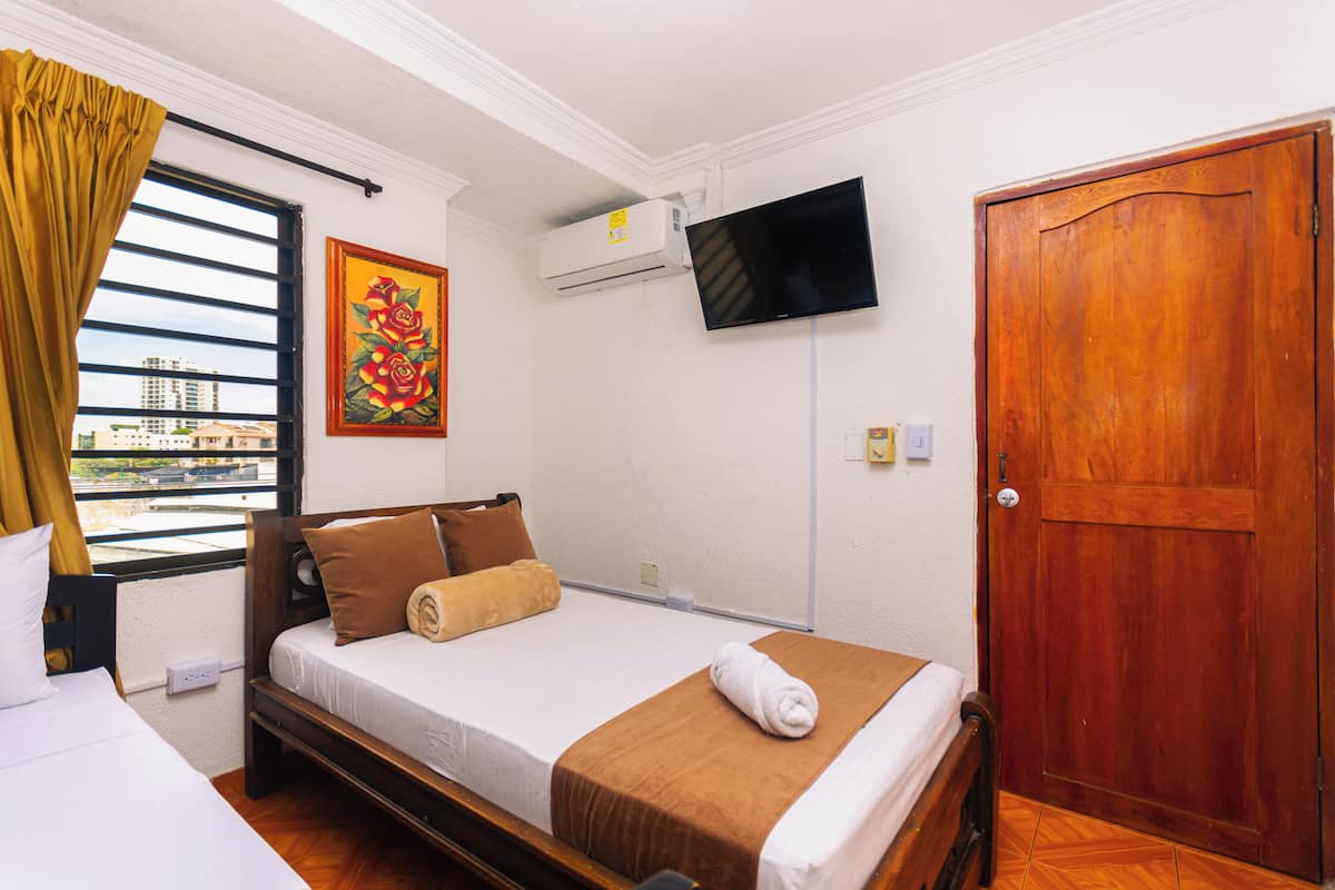 Una habitación de hotel con una cama, un televisor montado en la pared, una puerta de madera y una ventana con cortinas.