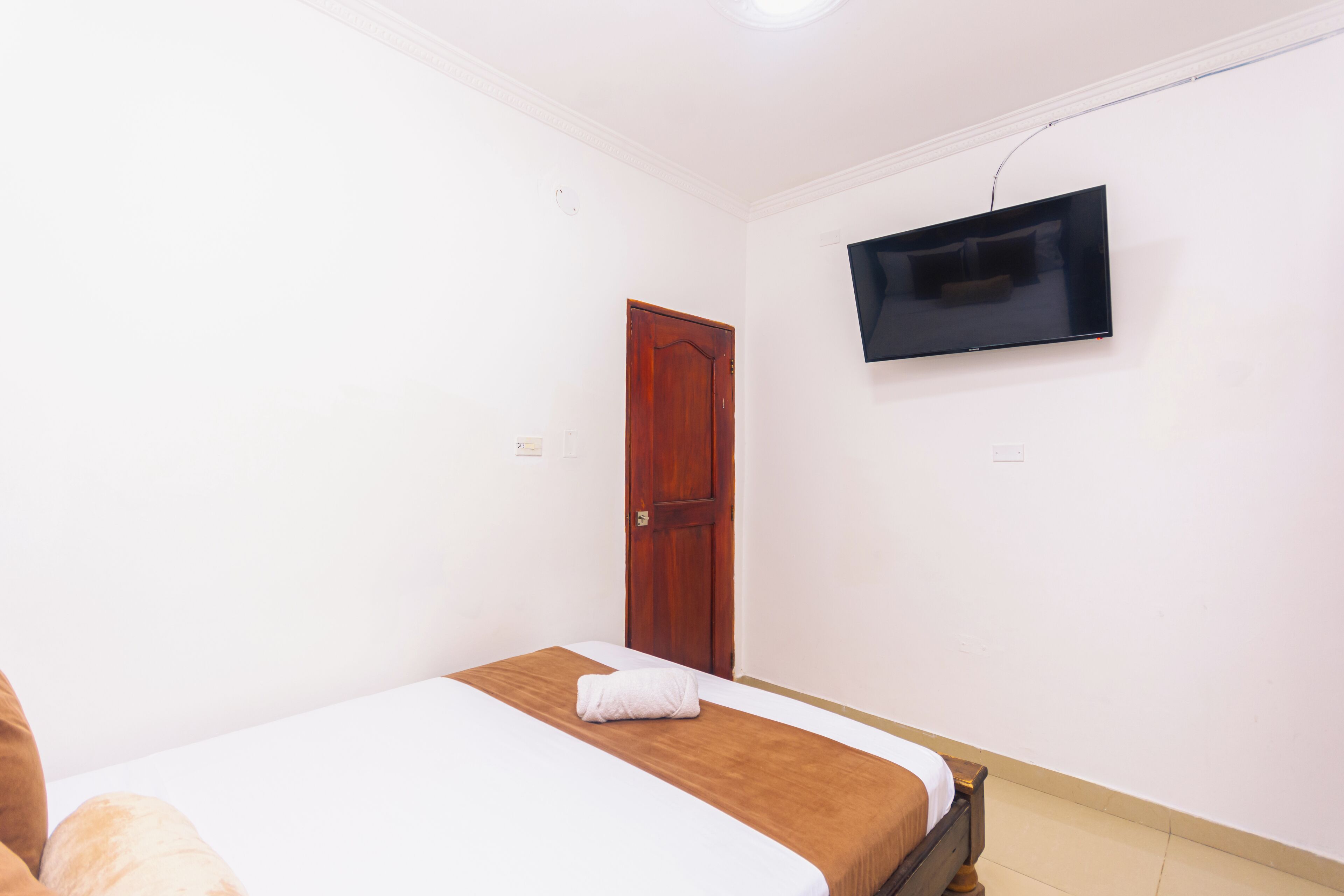 A bedroom with a single bed, a wooden door, and a mounted television.