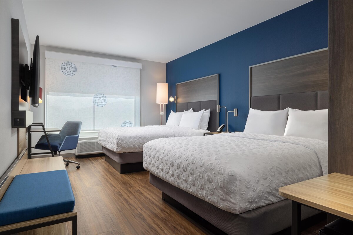 A hotel room with two beds, a desk, a chair, and a TV mounted on the wall.