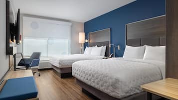 Ein Hotelzimmer mit zwei Betten, einem Schreibtisch, einem Stuhl und einem an der Wand befestigten Fernseher.