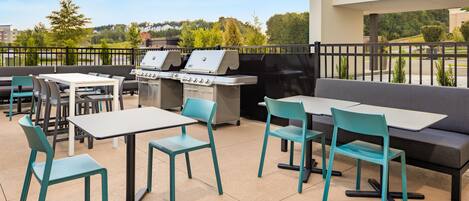 An outdoor patio with a barbecue grill, seating area, and tables.