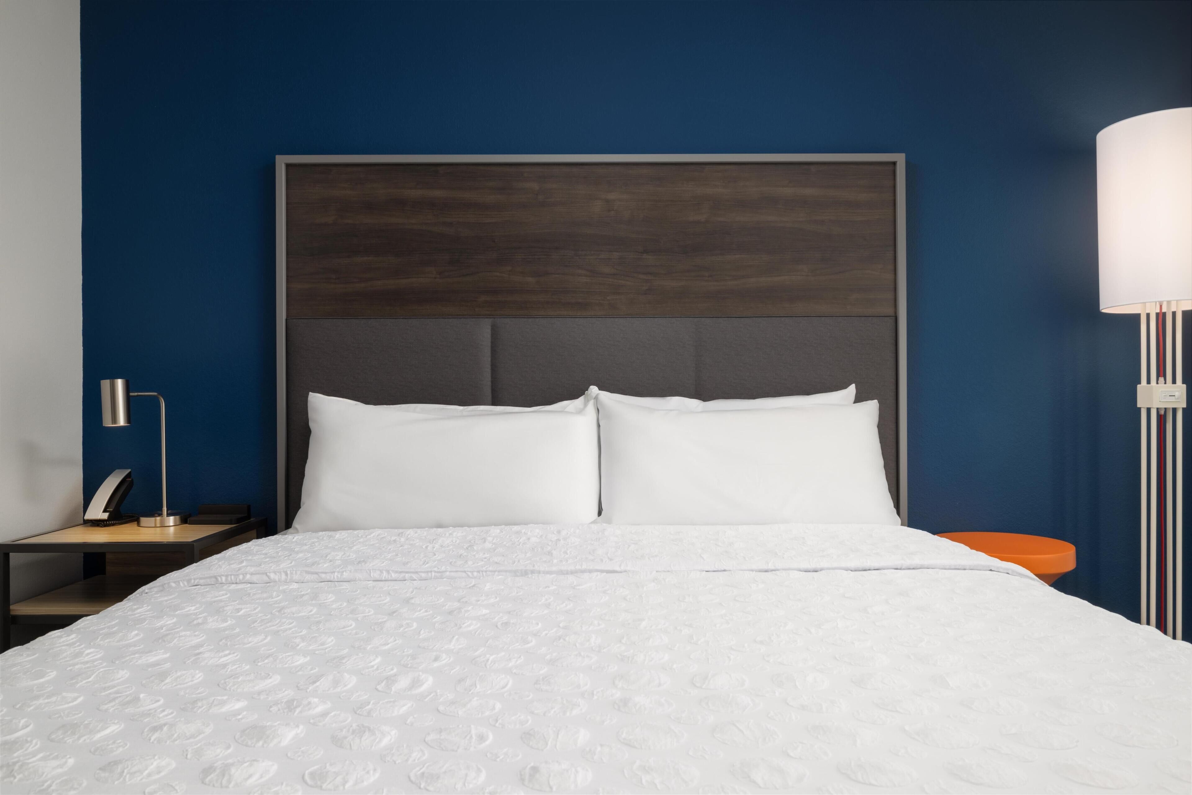 A hotel room with a large bed, a nightstand, a lamp, and a wall-mounted light fixture.