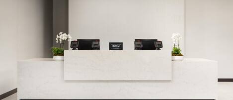 A clean, modern reception desk with two phones, a sign reading "Hilton Honors," and potted plants.