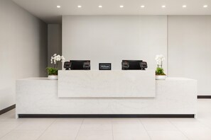 A clean, modern reception desk with two phones, a sign reading "Hilton Honors," and potted plants. - Tru By Hilton Cleveland, TN (Cleveland)