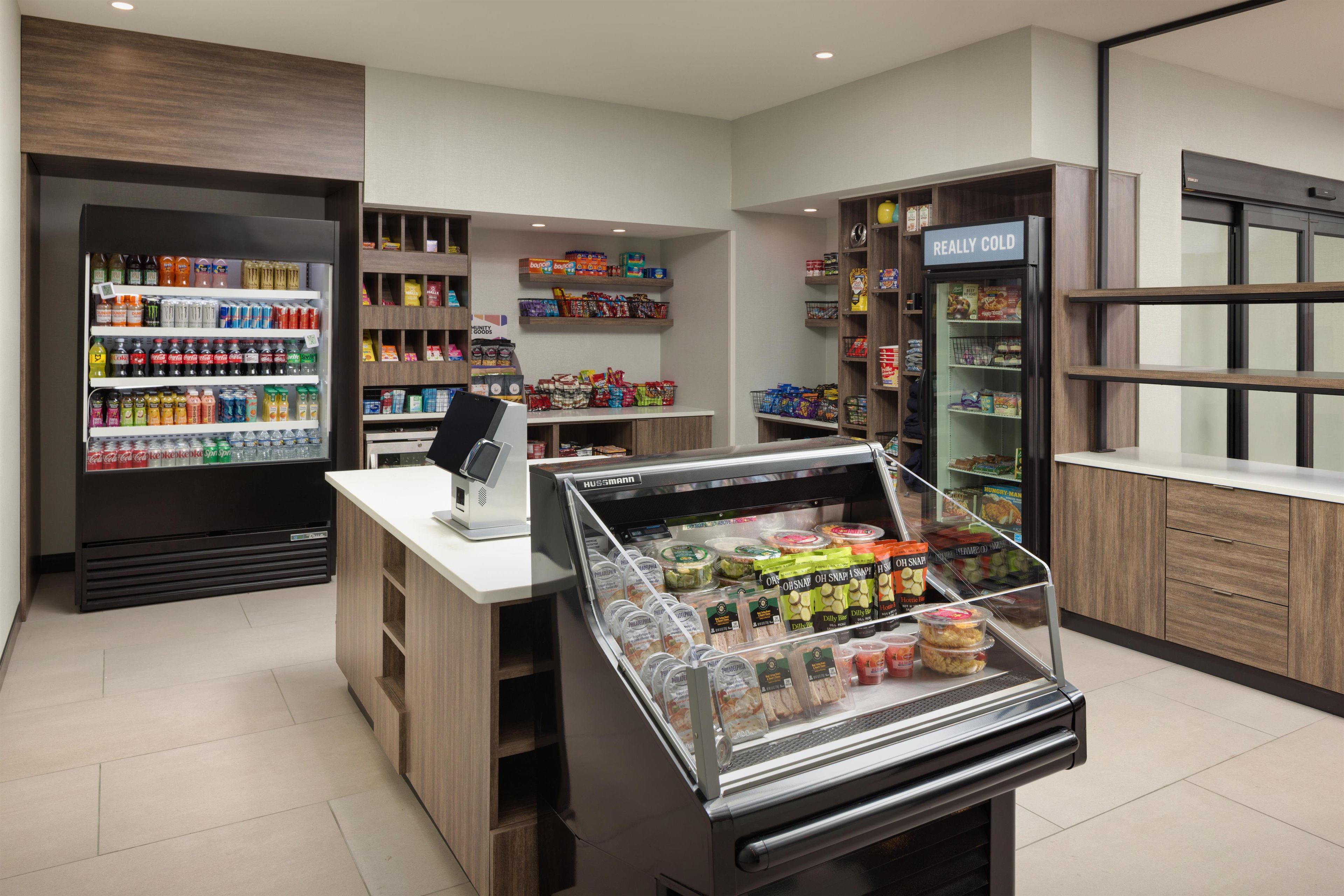Interior de una tienda de comestibles con secciones refrigeradas, estantes llenos de aperitivos y una zona de caja.