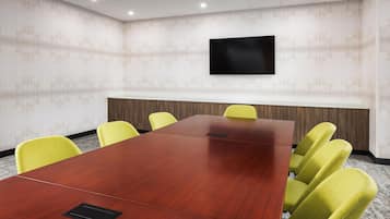 A conference room with a long wooden table, yellow chairs, a flat-screen TV mounted on the wall, and a whiteboard.