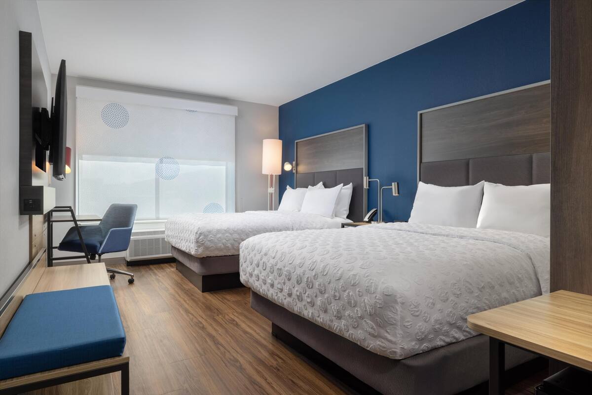 Una habitación de hotel con dos camas, un escritorio, una silla y un televisor montado en la pared.
