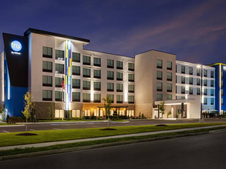 Un hotel moderno con un llamativo letrero de 'tru by Hilton', varios pisos y una entrada bien iluminada.