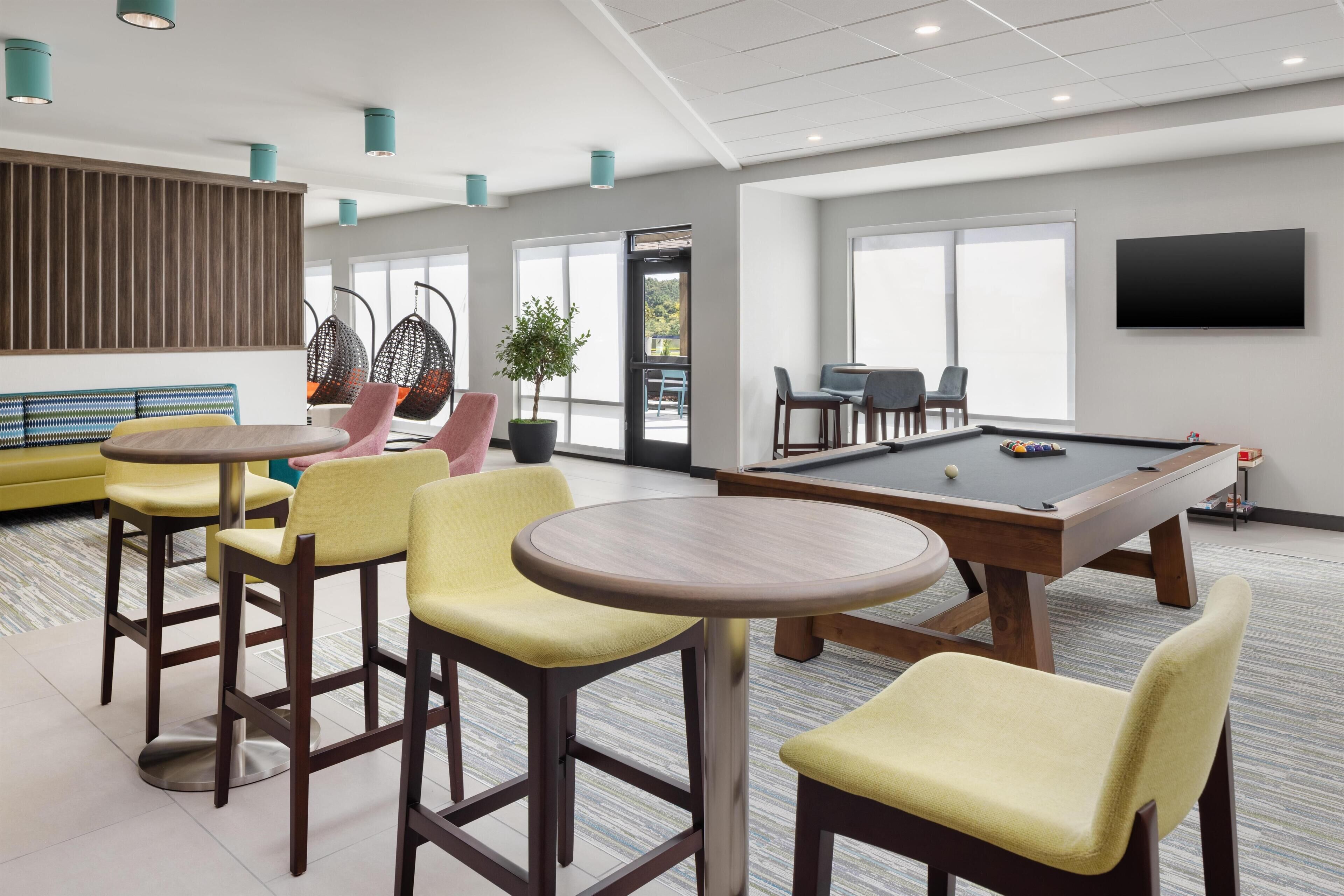 Een moderne lounge met een pooltafel, gele stoelen, een bank en een aan de muur bevestigde televisie.