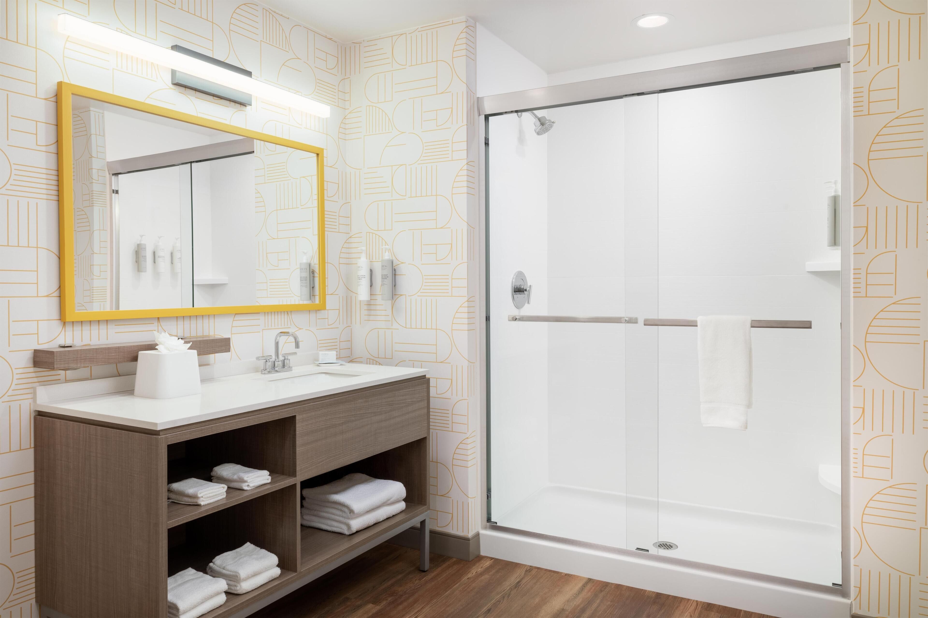 A modern bathroom with a wooden vanity, a large mirror, and a glass-enclosed shower.