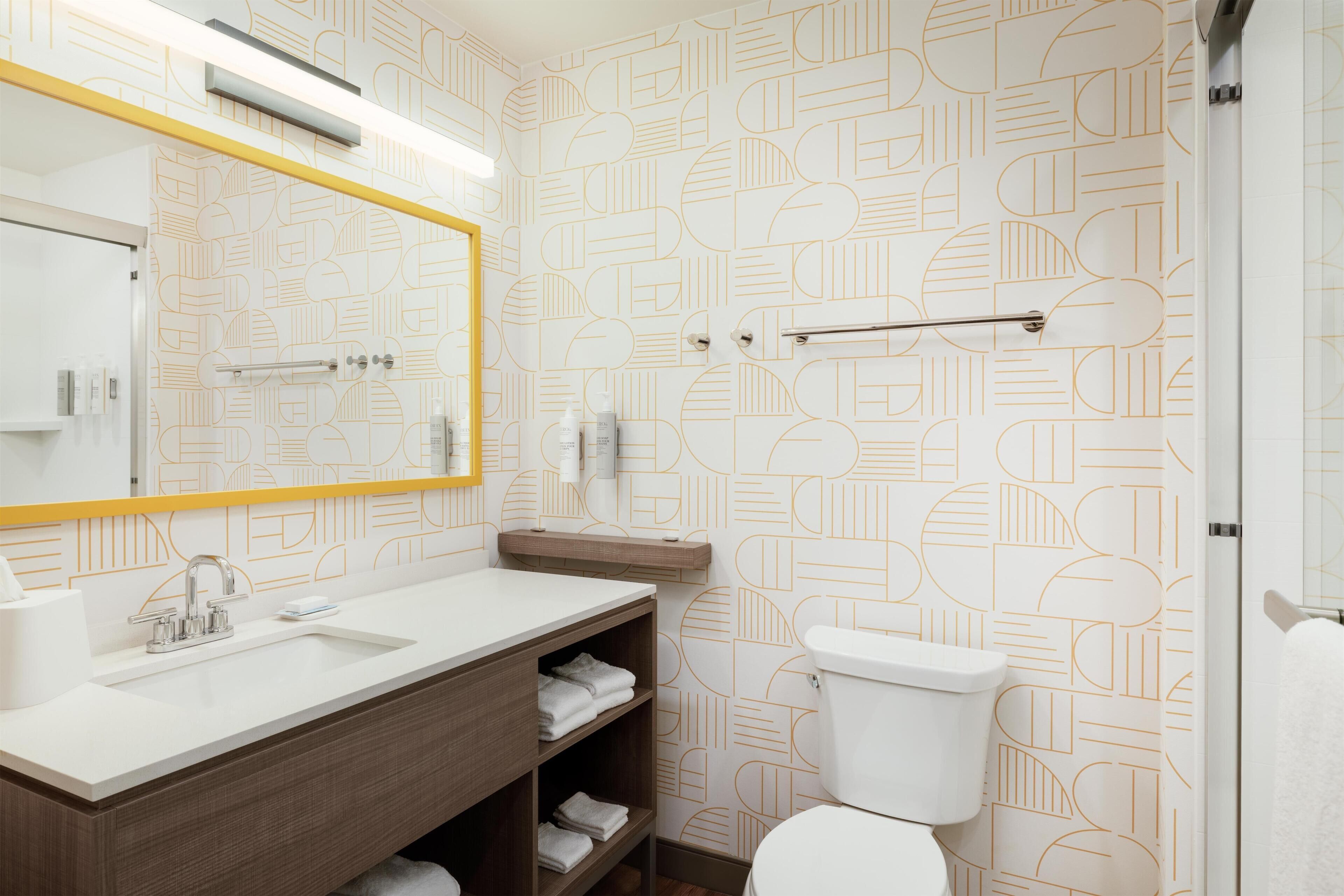 A modern bathroom with a geometric patterned wall, a white sink, a mirror with a yellow frame, and a toilet.