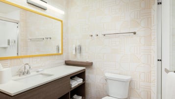 A modern bathroom with a geometric patterned wall, a white sink, a mirror with a yellow frame, and a toilet.