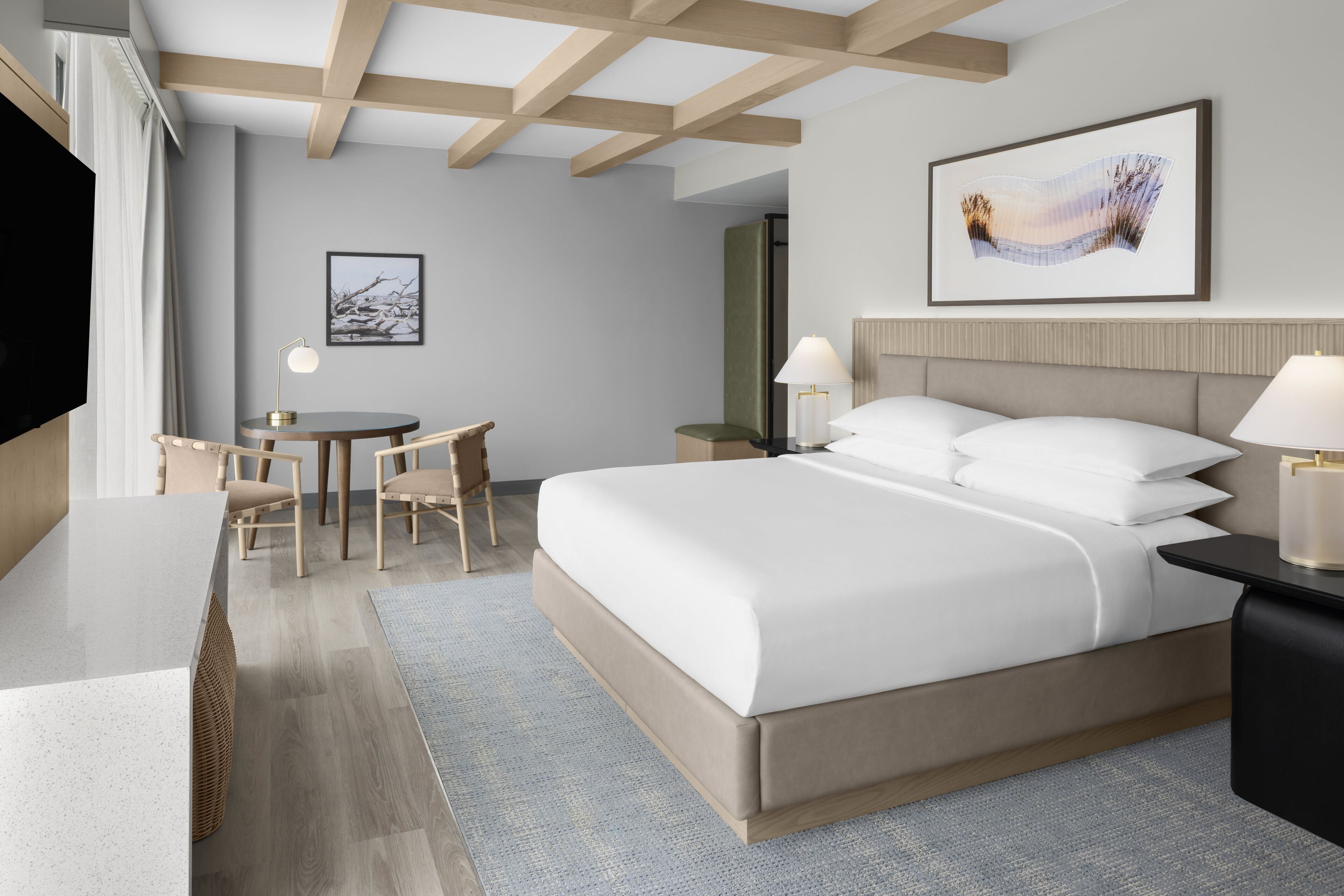 A modern hotel room with a large bed, a desk with a chair, a small table, and a television.