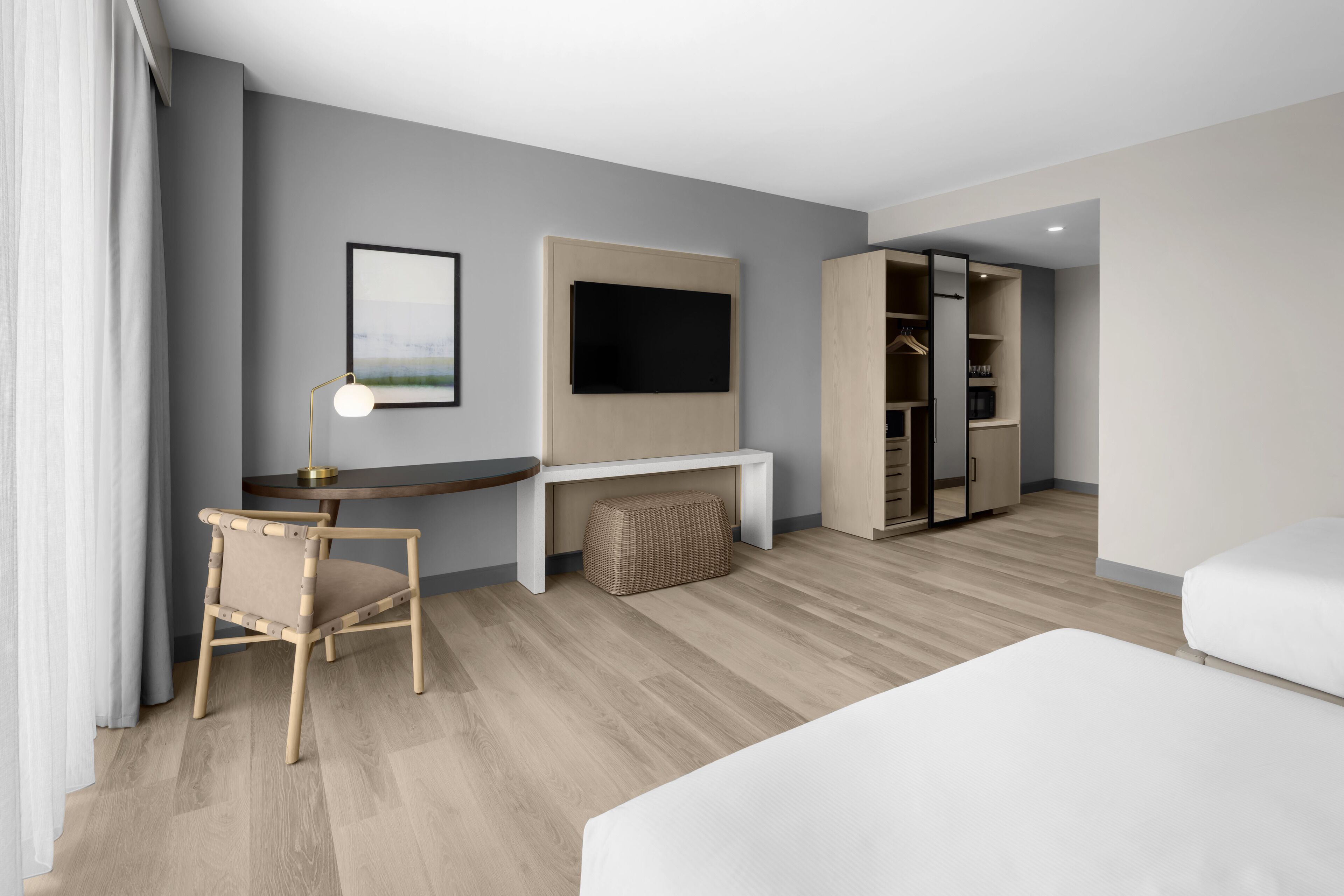 A modern hotel room with a bed, a desk with a chair, a TV mounted on the wall, and a walk-in closet.
