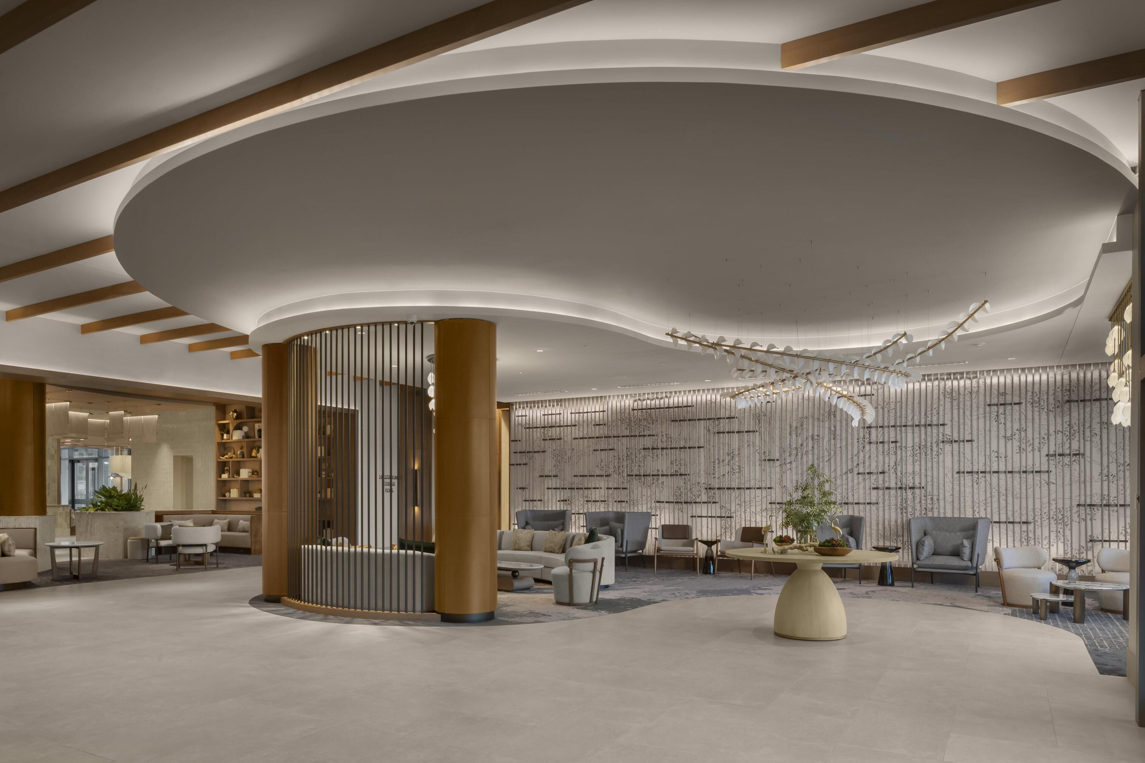 Un hall d’entrée spacieux doté d’un plafond incurvé, d’une colonne centrale et d’un espace détente avec des canapés et des fauteuils.