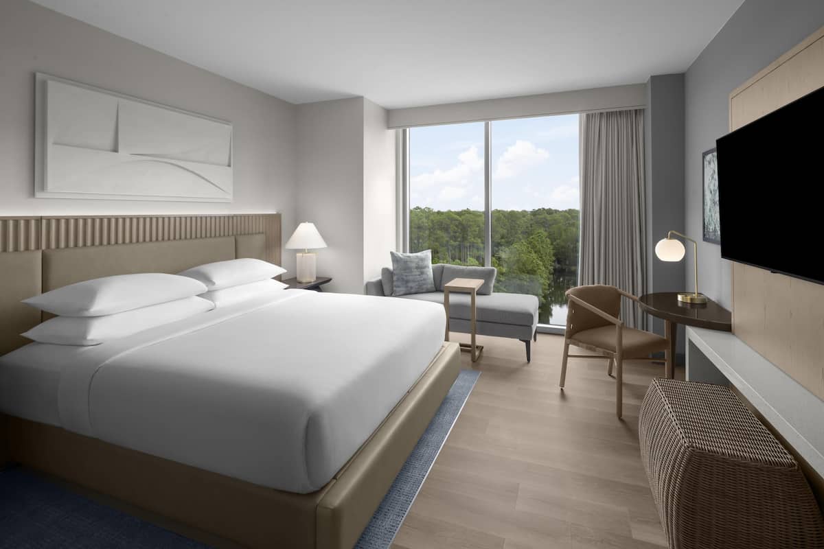 A modern hotel room with a large bed, a desk, a chair, and a TV.