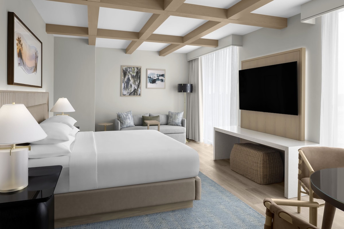 A modern hotel room with a large bed, a TV, a sofa, and a desk.