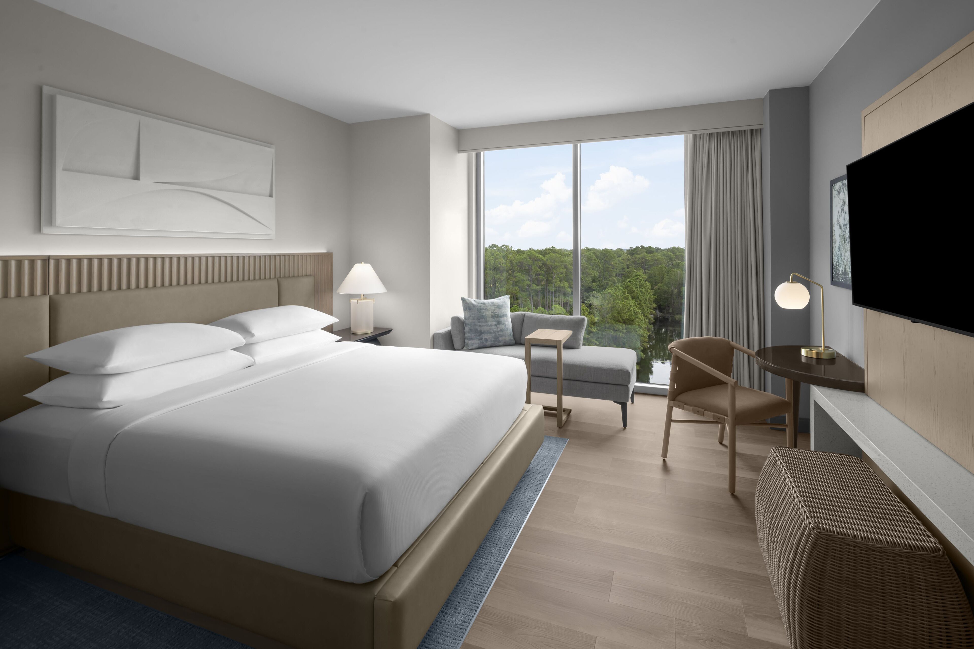 A modern hotel room with a large bed, a desk, a chair, and a TV.