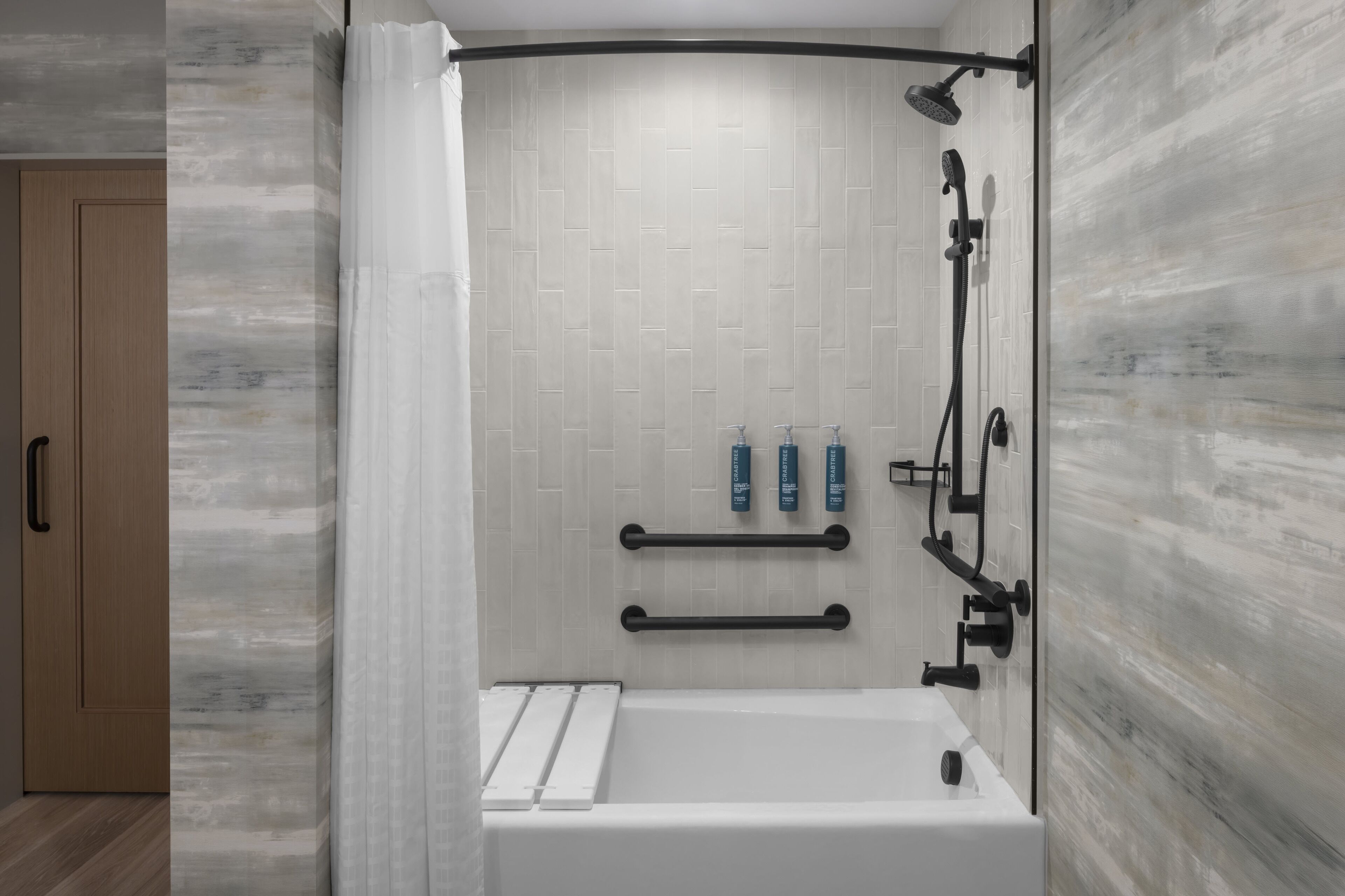 A modern bathroom with a bathtub, shower, and handrails.