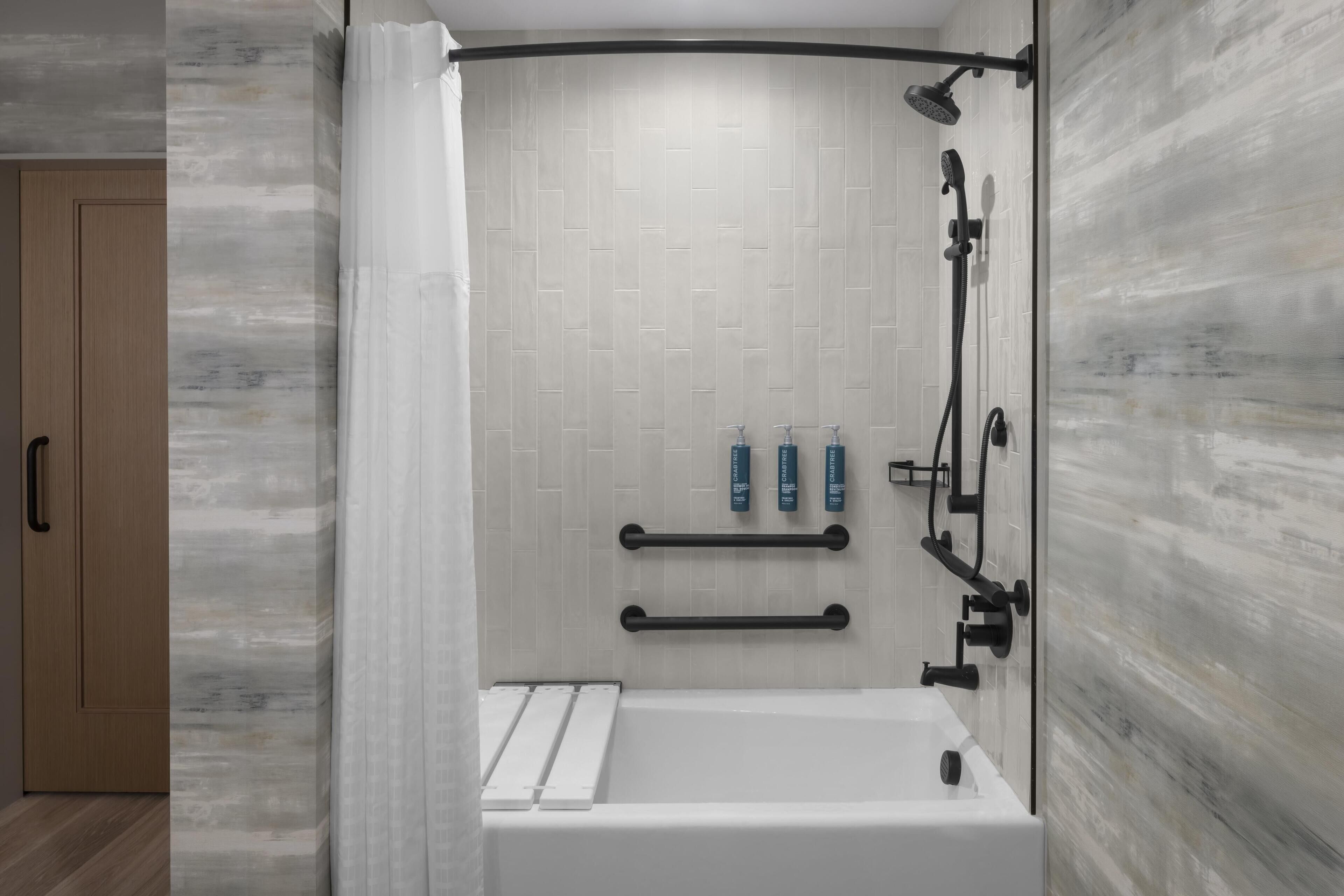 A modern bathroom with a bathtub, shower, and handrails.