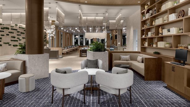 Un moderno vestíbulo con una zona de estar central, estanterías de madera con objetos decorativos y un pilar grande.