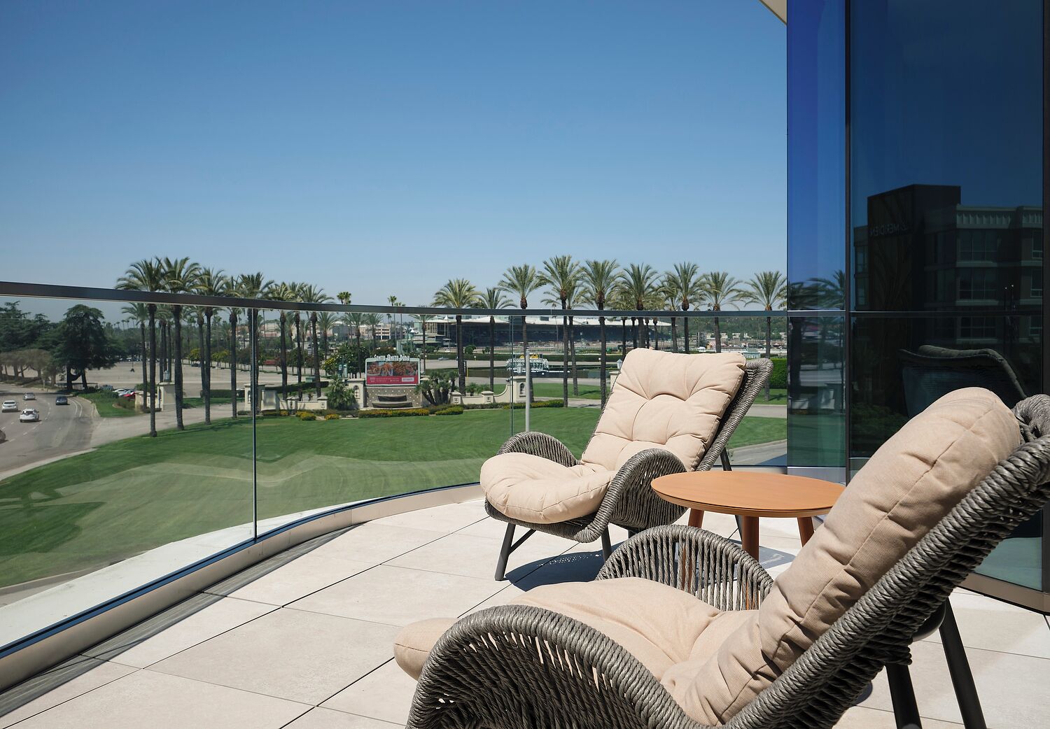 A balcony with wicker furniture, a glass railing, and a view of a golf course and palm trees.