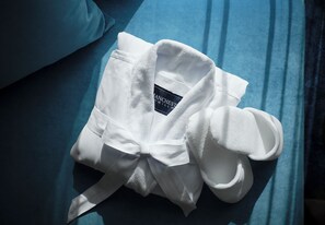 A white bathrobe with a label on a blue bedspread. - Hilton Arcadia Pasadena Area (Arcadia)