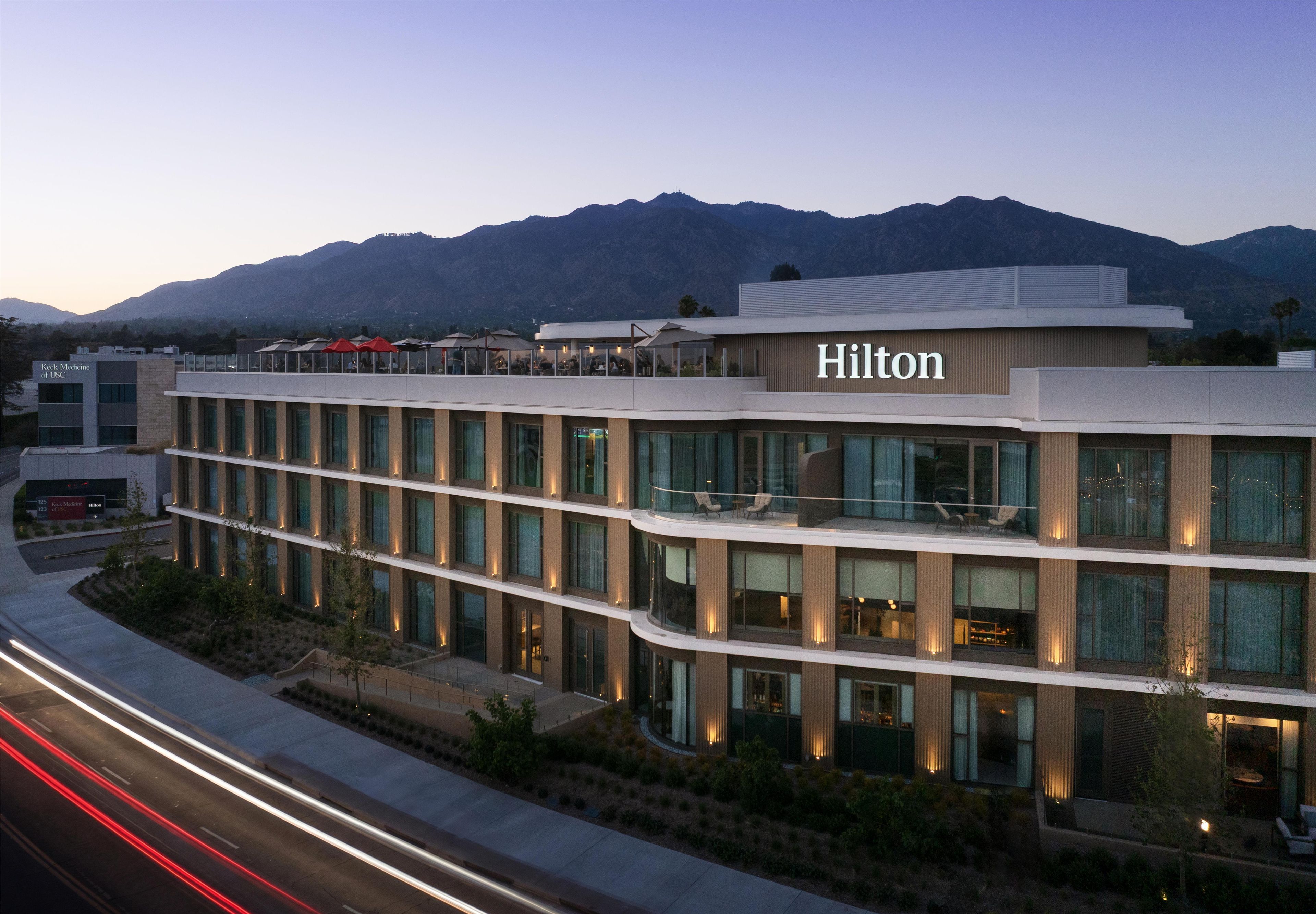 Un hotel de varios pisos con un llamativo letrero de 'Hilton', rodeado de montañas y con un diseño arquitectónico moderno.