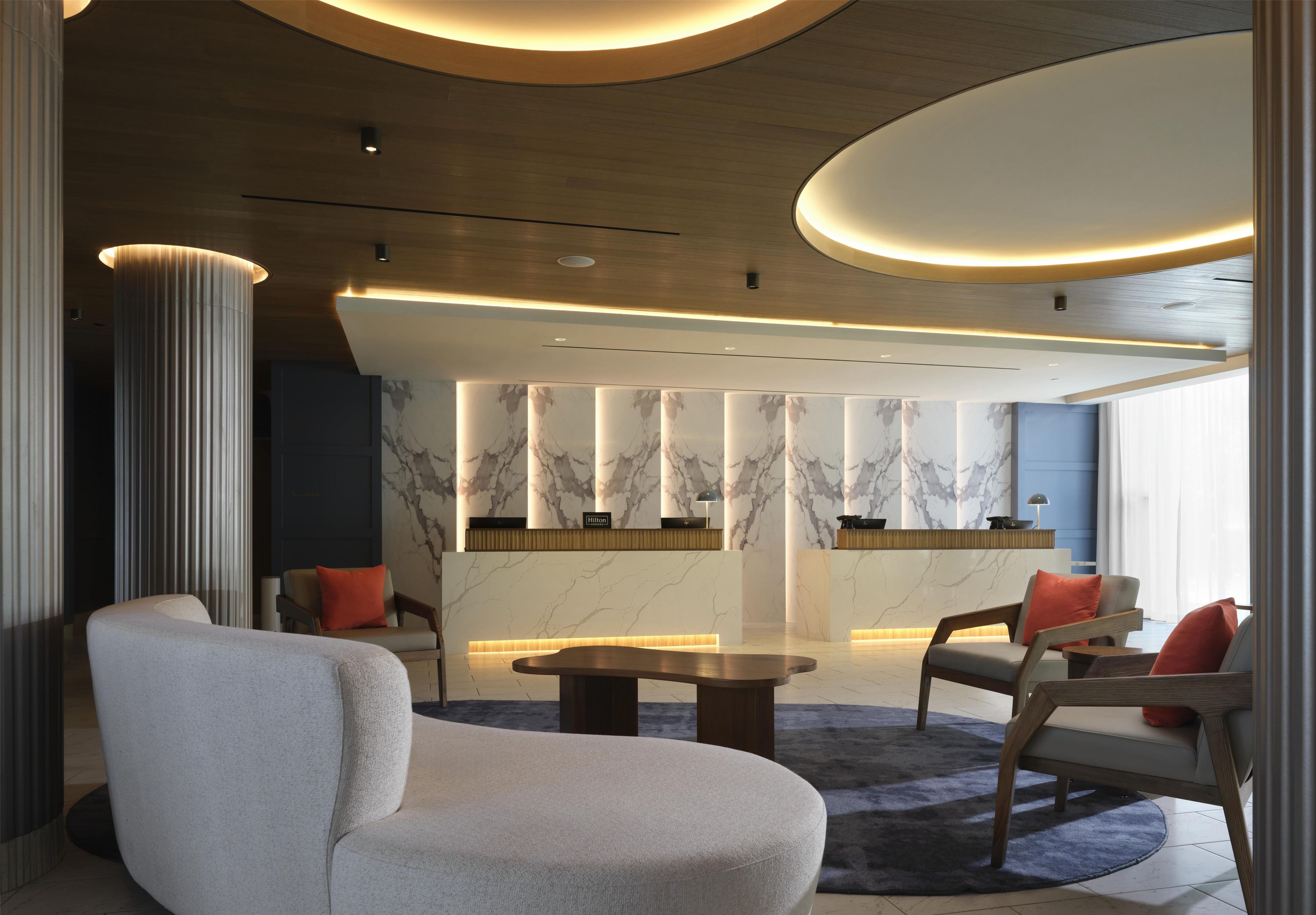 Un hall d’entrée moderne avec un comptoir de réception en marbre, un espace salon avec des canapés et une table basse.