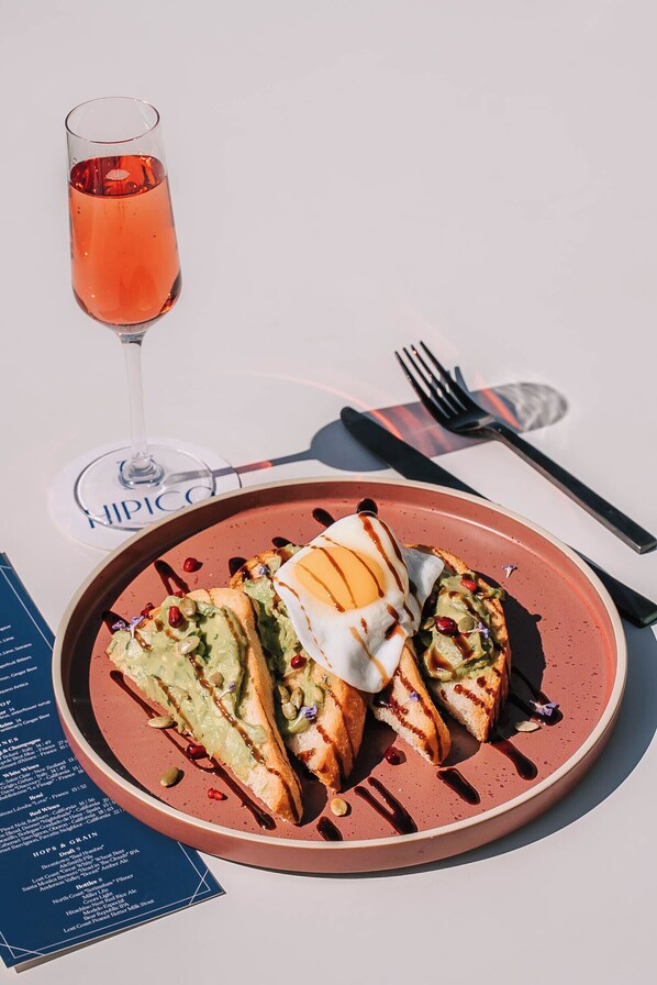 A plate with a sandwich and a glass of pink beverage on a table with a menu. - Hilton Arcadia Pasadena Area (Arcadia)