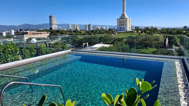 A rooftop pool with clear water, surrounded by greenery and overlooking a cityscape with modern buildings and a prominent tower. - Hotel Hampton by Hilton Santiago de los Caballeros (Santiago de los Caballeros)